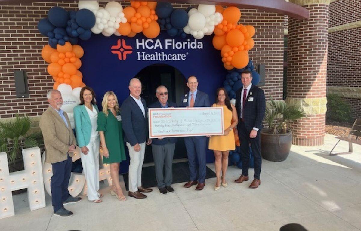Well-dressed people holding a giant check, with balloons festooned over an entrance way.