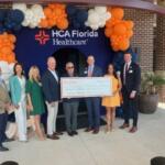 Well-dressed people holding a giant check, with balloons festooned over an entrance way.