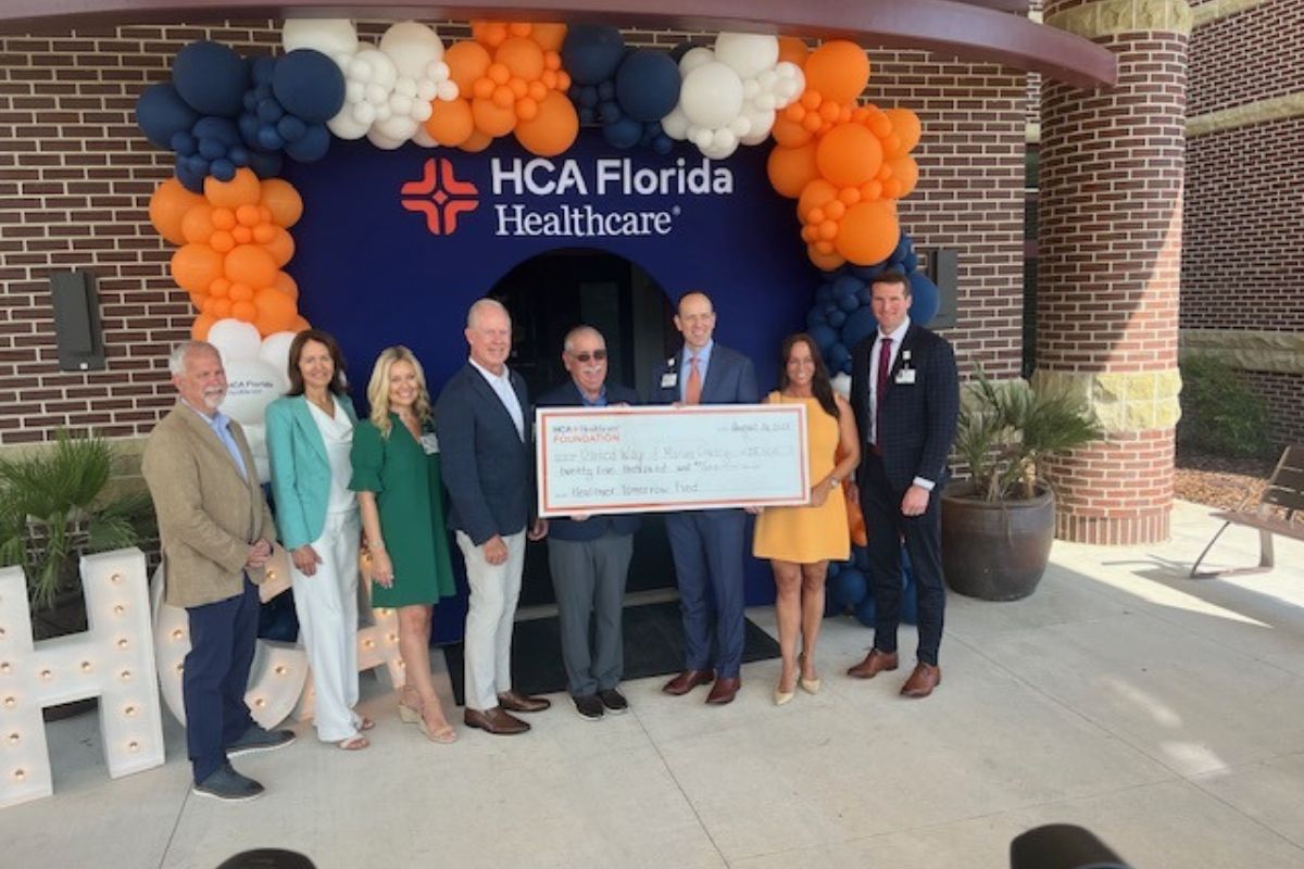Well-dressed people holding a giant check, with balloons festooned over an entrance way.