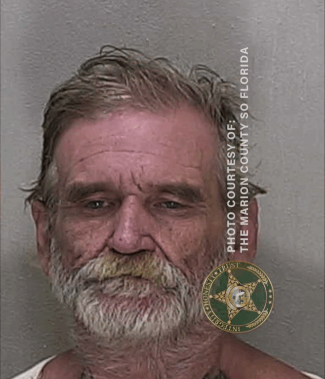 Mugshot of an older man with gray hair and a beard, wearing an orange jail uniform, looking directly at the camera.