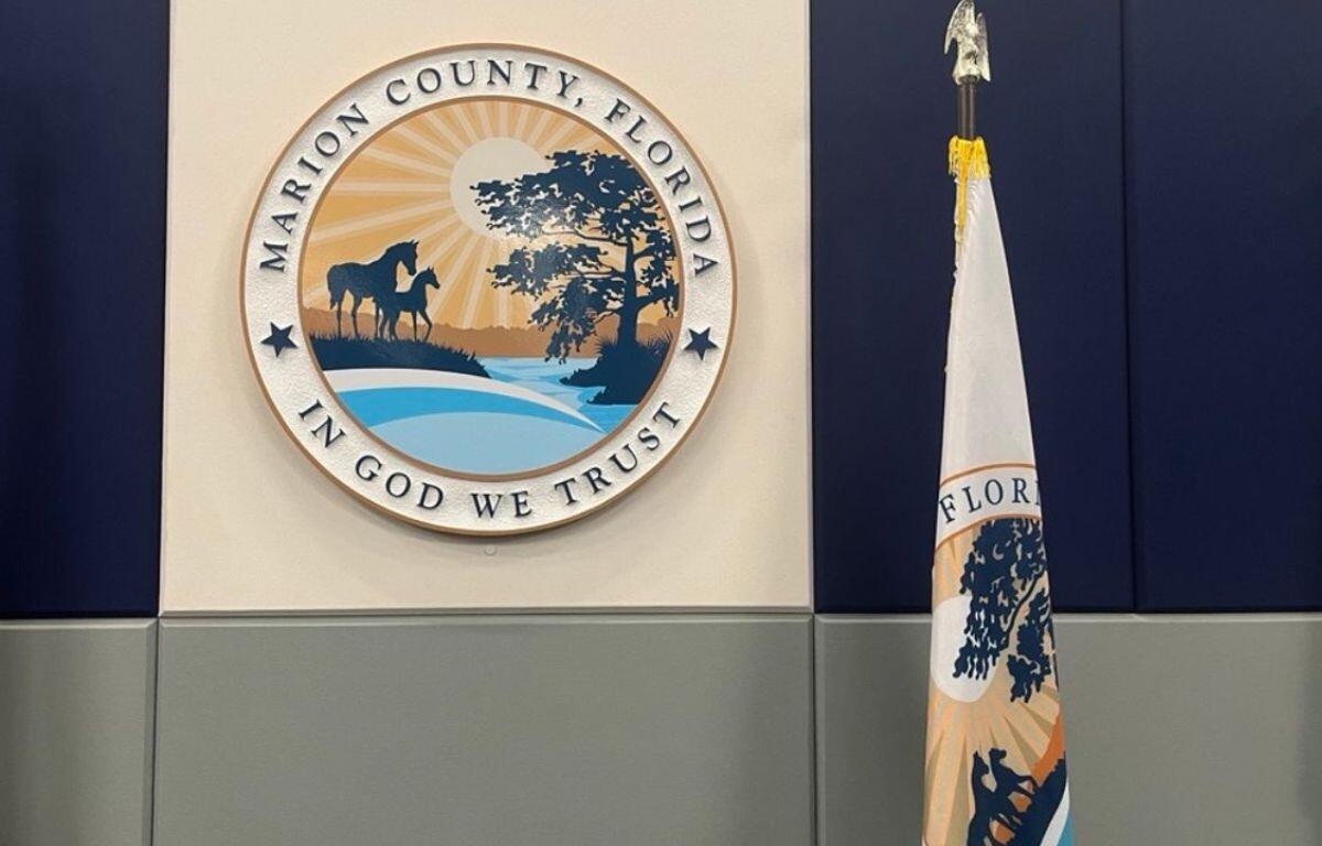 A beige background, with a circle with an insignia featuring lettering and a landscape image, with a flag to the right, and at the bottom and gray coloring at the bottom of the wall.