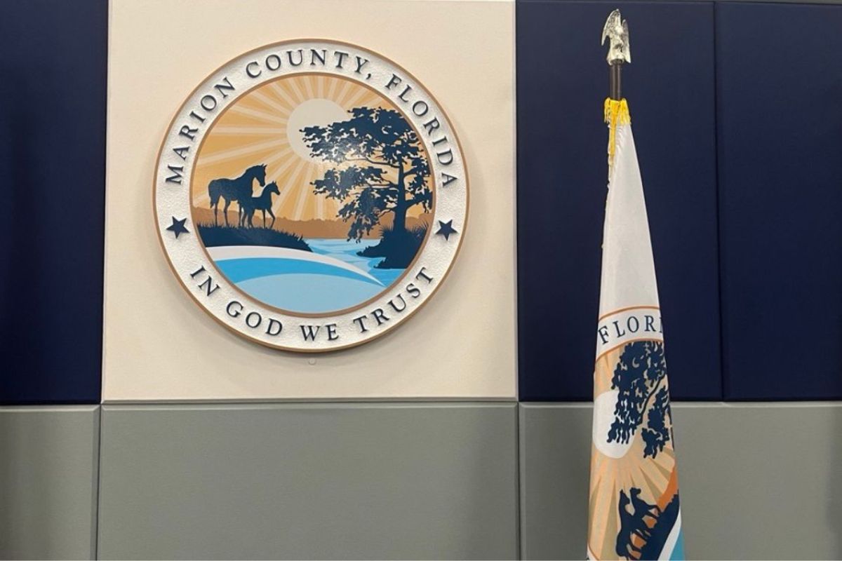 A beige background, with a circle with an insignia featuring lettering and a landscape image, with a flag to the right, and at the bottom and gray coloring at the bottom of the wall.