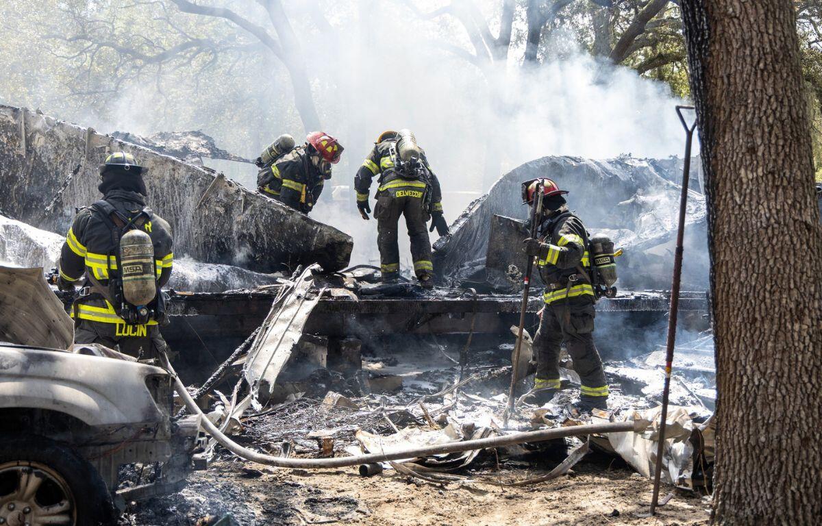 Firefighters in full gear work amid heavy smoke and debris at the site of a house fire.