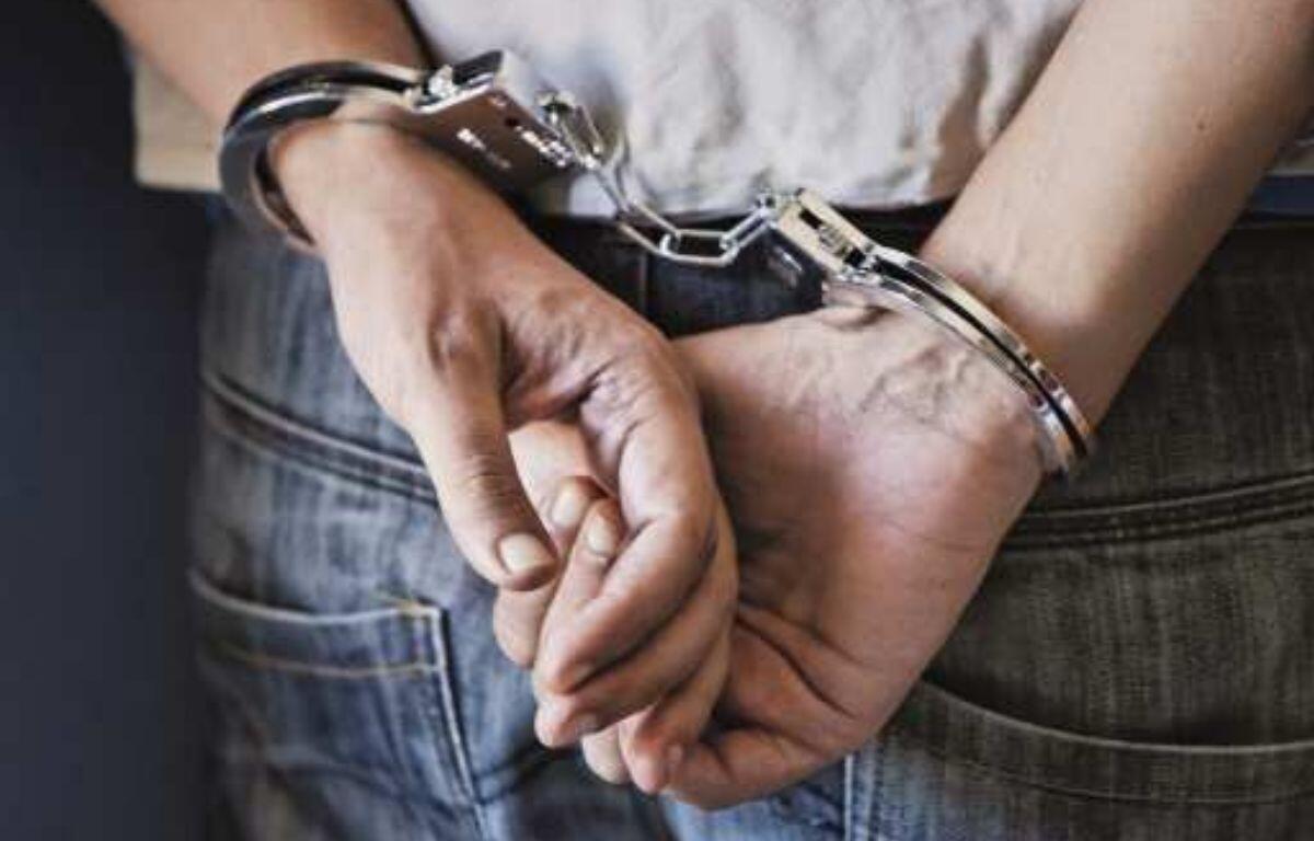 A close-up photo of a person’s hands cuffed together with metal handcuffs, resting on their lap.
