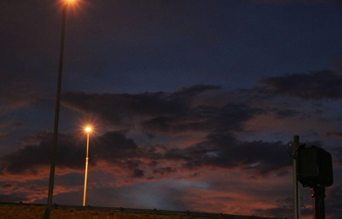 Streetlights cast a warm glow against a dark blue and purple sky as scattered clouds loom overhead.