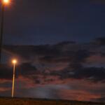 Streetlights cast a warm glow against a dark blue and purple sky as scattered clouds loom overhead.