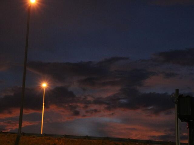Streetlights cast a warm glow against a dark blue and purple sky as scattered clouds loom overhead.