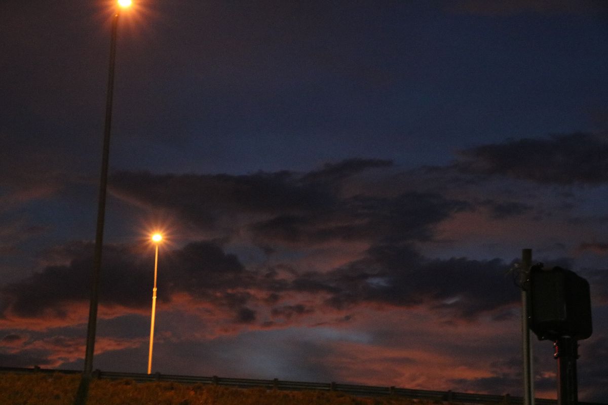 Streetlights cast a warm glow against a dark blue and purple sky as scattered clouds loom overhead.