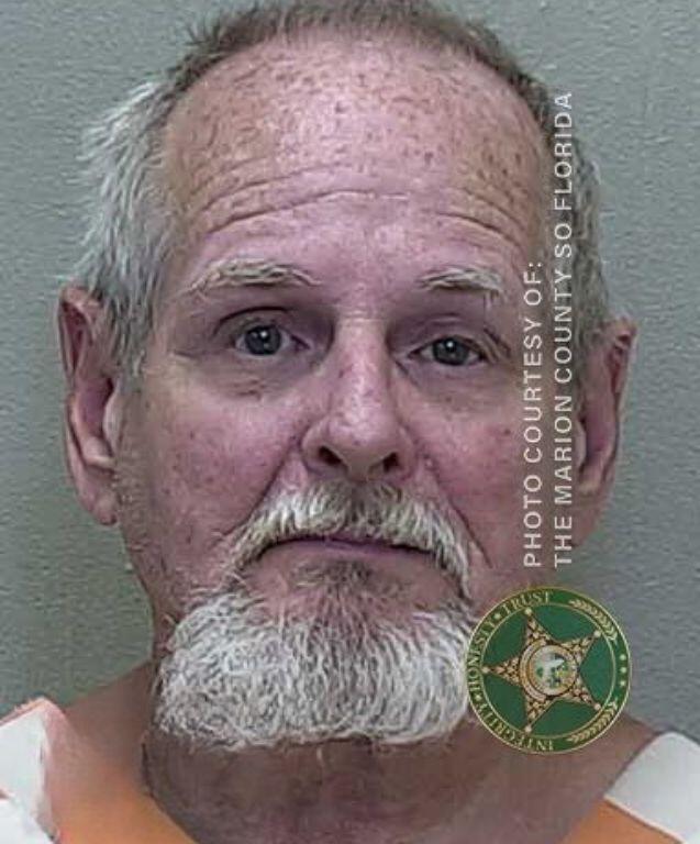 Mugshot of an older man with a bald head and white beard, wearing an orange-and-white striped prison uniform.