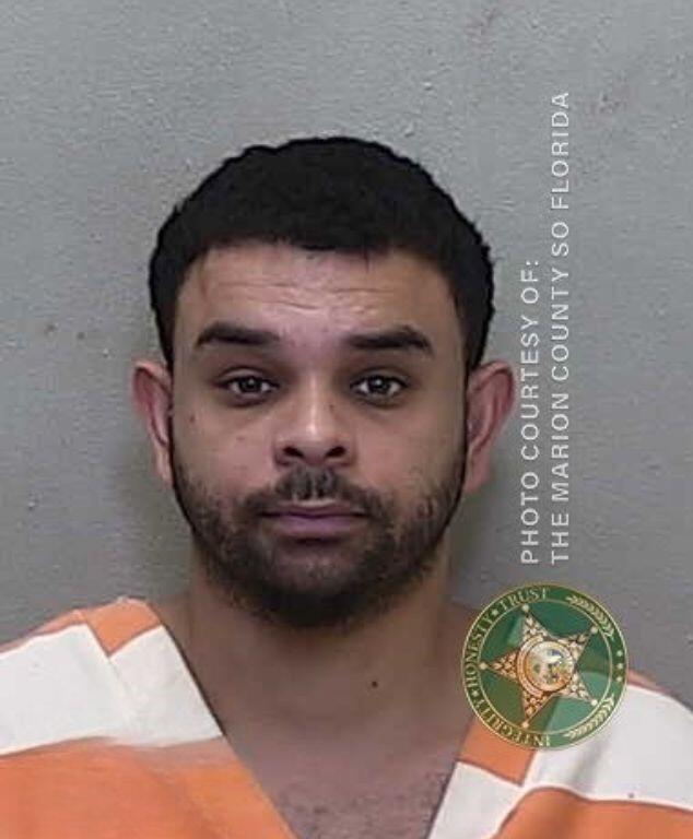 Mugshot of a man wearing an orange-and-white jail uniform, looking straight at the camera with a neutral expression.