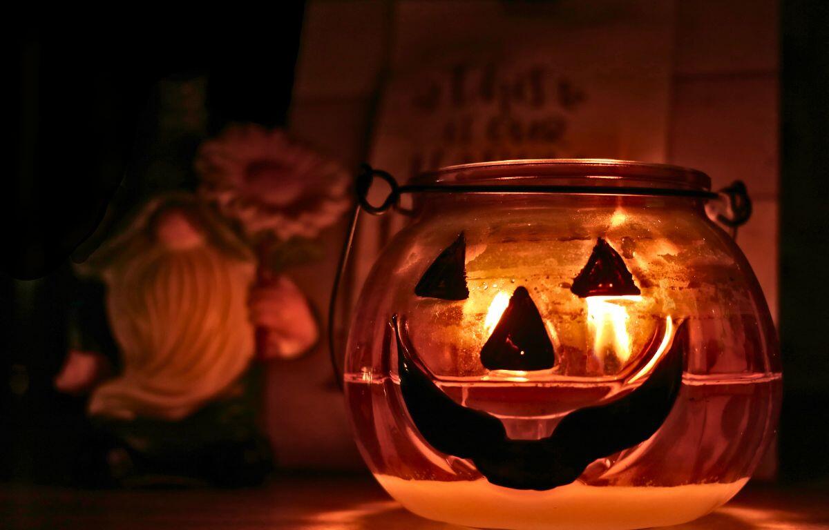 A pumpkin candle lit and glowing in the foreground with a gnome and sign in the background.