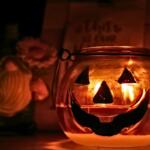 A pumpkin candle lit and glowing in the foreground with a gnome and sign in the background.