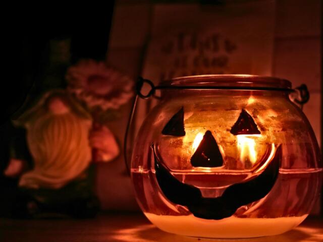 A pumpkin candle lit and glowing in the foreground with a gnome and sign in the background.