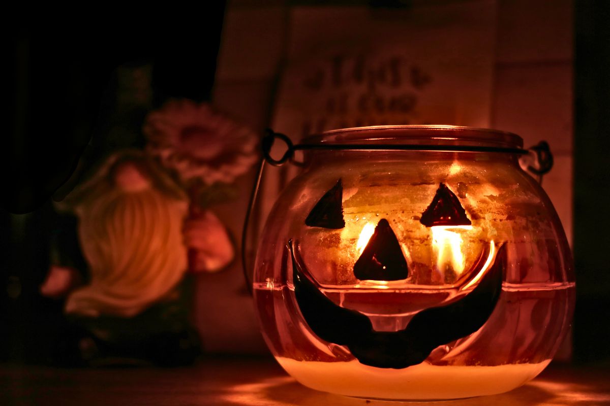 A pumpkin candle lit and glowing in the foreground with a gnome and sign in the background.