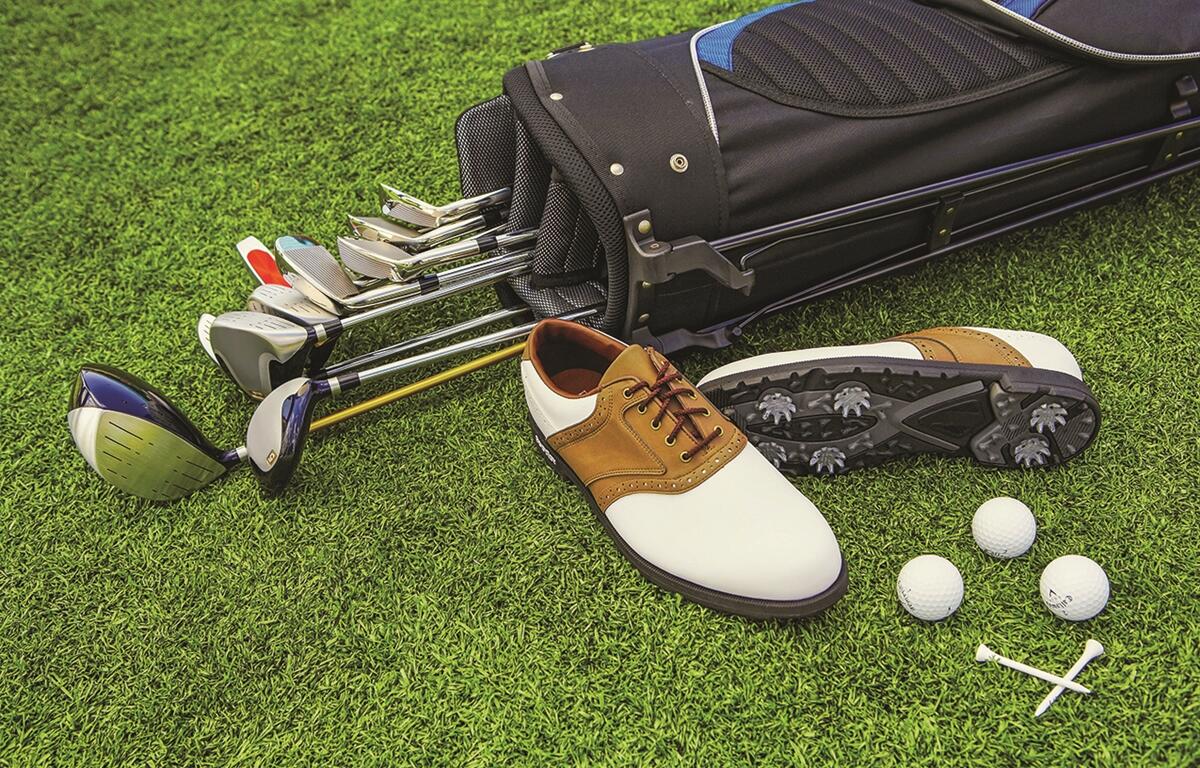 Golf clubs, shoes, balls, and tees on green grass at a golf course.