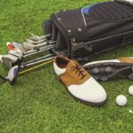 Golf clubs, shoes, balls, and tees on green grass at a golf course.