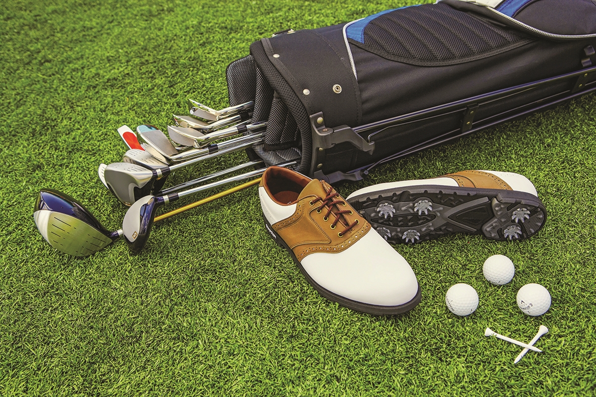 Golf clubs, shoes, balls, and tees on green grass at a golf course.