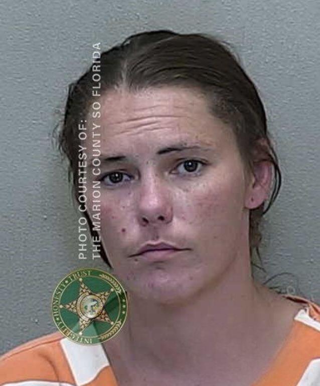 Mugshot of a woman with dark hair pulled back, wearing an orange-and-white striped prison uniform.