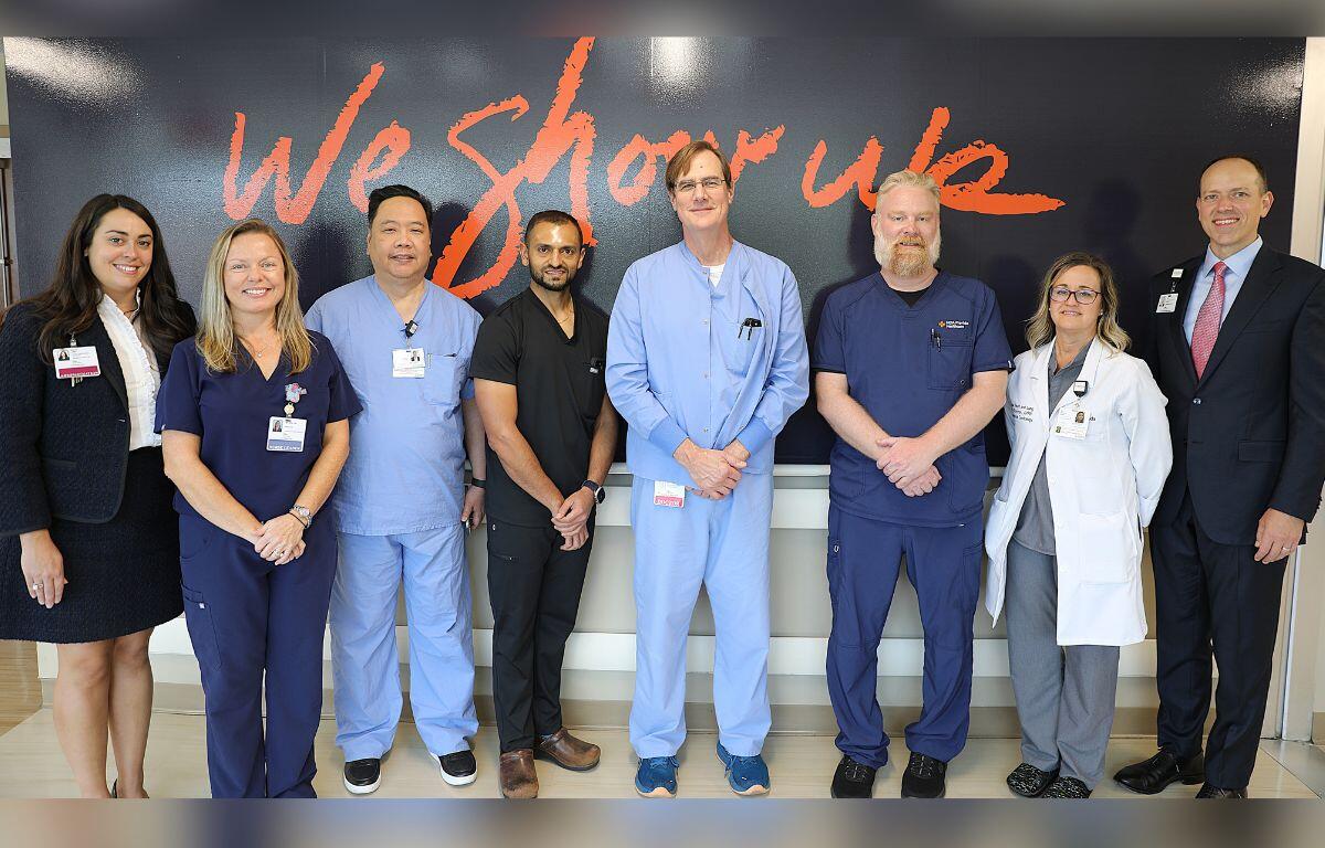 A well-dressed woman in business attire, with men and women dressed in scrubs, with a woman on the far right wearing a doctor's smock, with the gentleman on the extreme right wearing a well-tailoired suit.