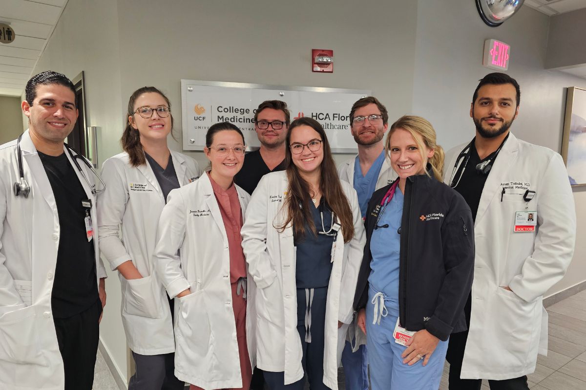 A group of men and women wearing doctors smocks and scrubs standing against a wall.