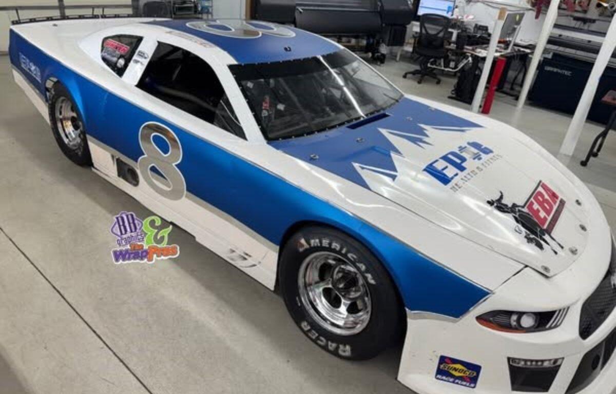 A white and blue race car with a large "8" decal on the side is parked inside a workshop.