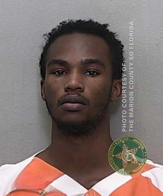Mugshot of a young man in an orange-and-white jail uniform, facing the camera with a serious expression.