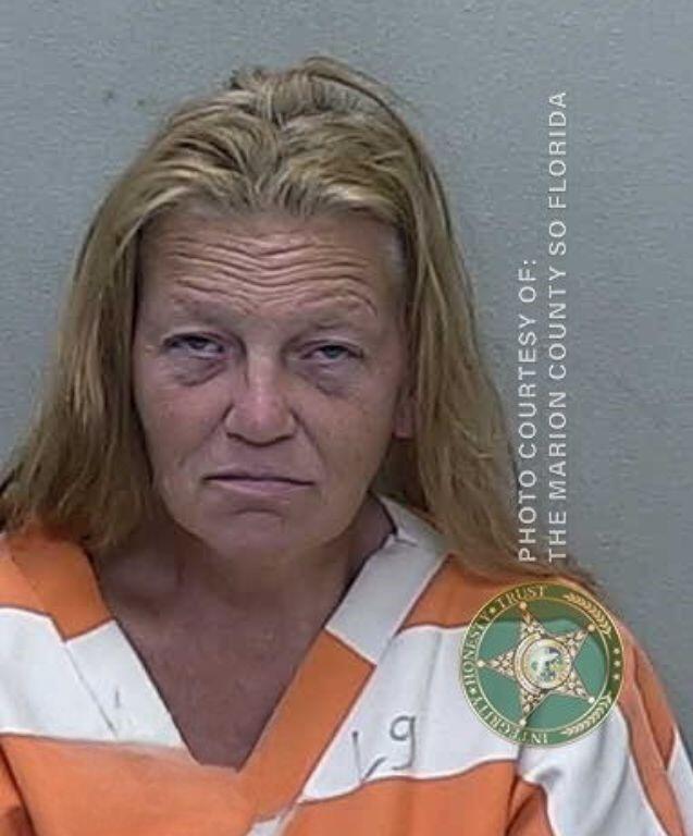 Mugshot of a woman with light brown hair, slightly disheveled, wearing an orange-and-white striped prison uniform.