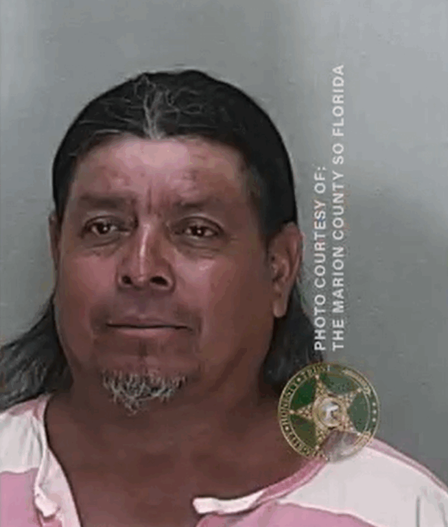 Mugshot of a man with long dark hair pulled back, wearing a two-toned jail uniform, looking directly at the camera.