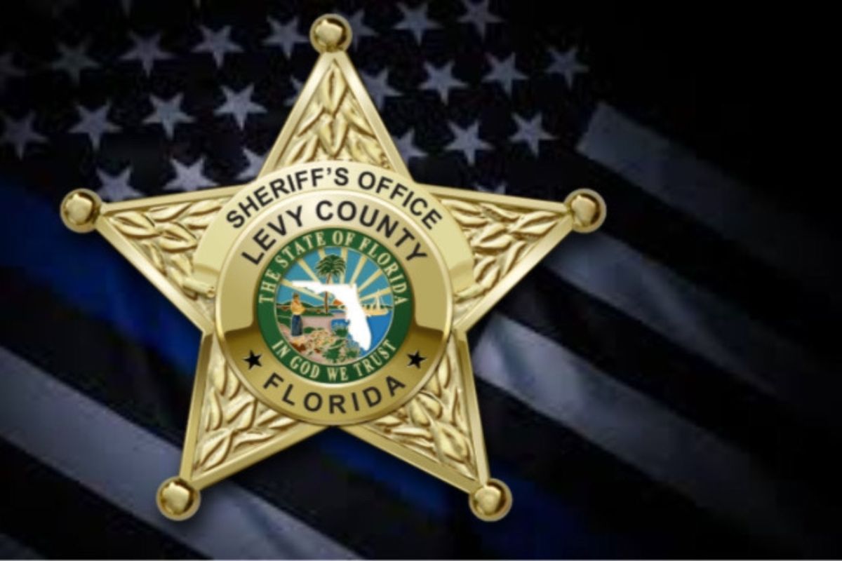 A gold badge, with writing and an insignia in the center of the badge against the background of the flag of the United States of America.