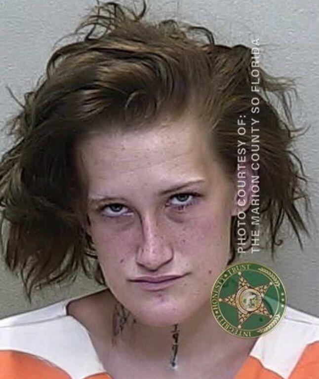 Mugshot of a woman in an orange-and-white jail uniform, with messy hair and a stern look on her face.