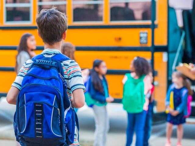 Children with backpacks stand near a yellow school bus on the first day of school.
