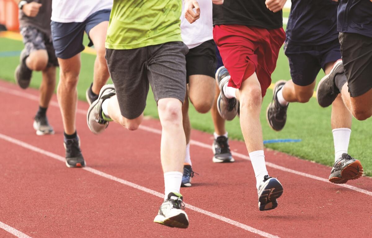 Close-up of runners' legs as they race on a red track.