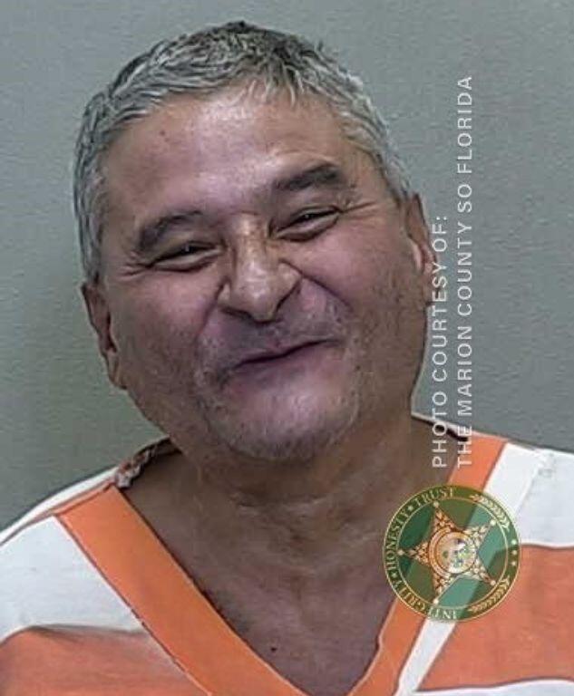 Mugshot of a man in an orange-and-white jail uniform, slightly tilting his head with a faint smirk.