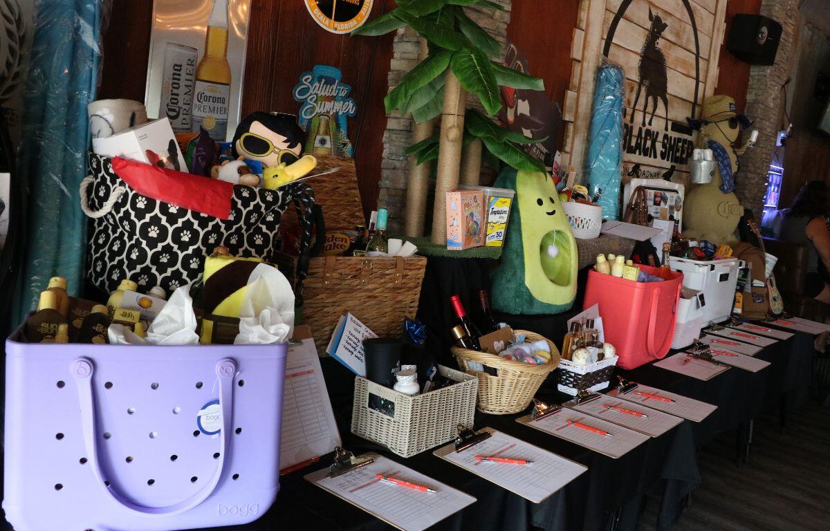A table lined with various animal food, treats, beds and more are mixed with various items. Clipboards with paper and pens sit at the edge of the table.