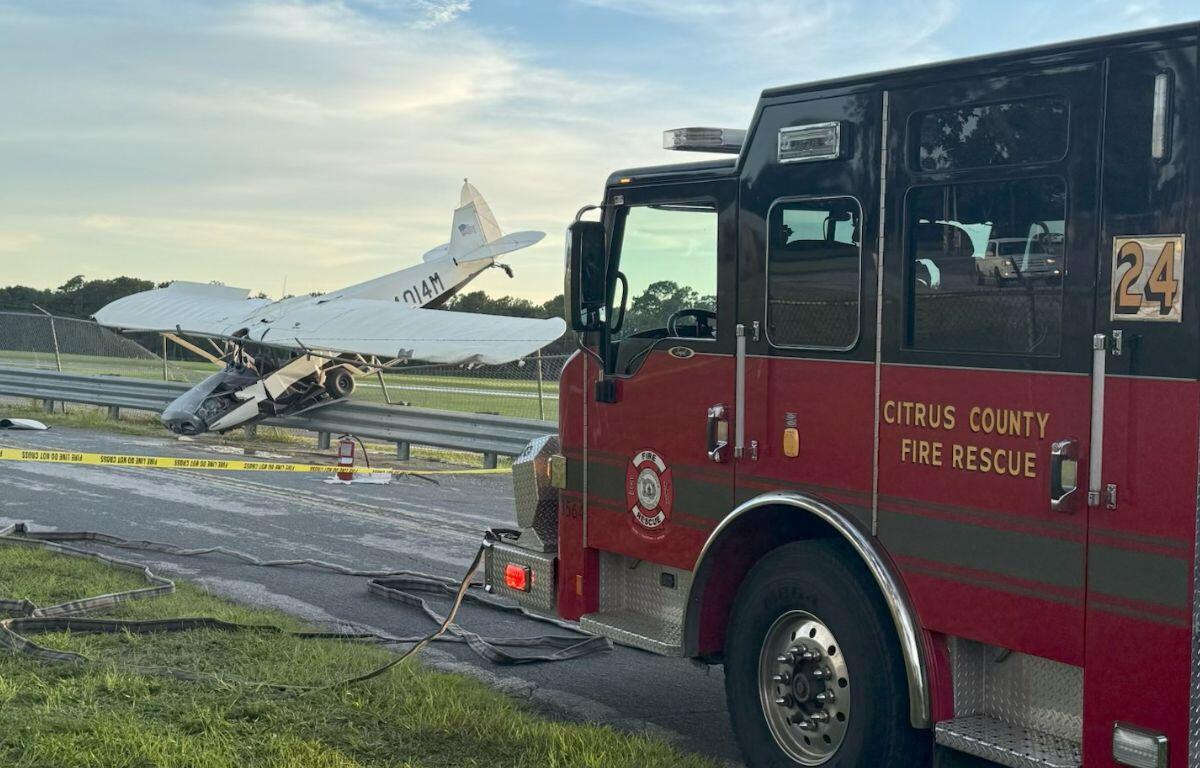 A plane resting on a berm in the background, with a roadway and grass in the foreground, to the right a fire engine.
