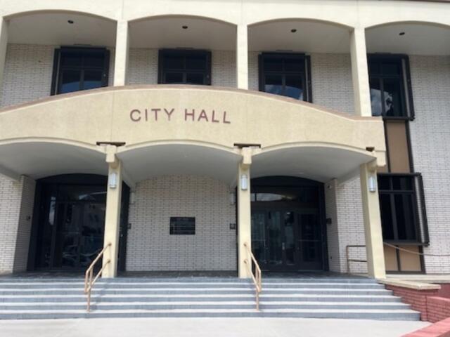 A building, with white trim, columns, a facade with lettering and steps leading toward the glass front doors.
