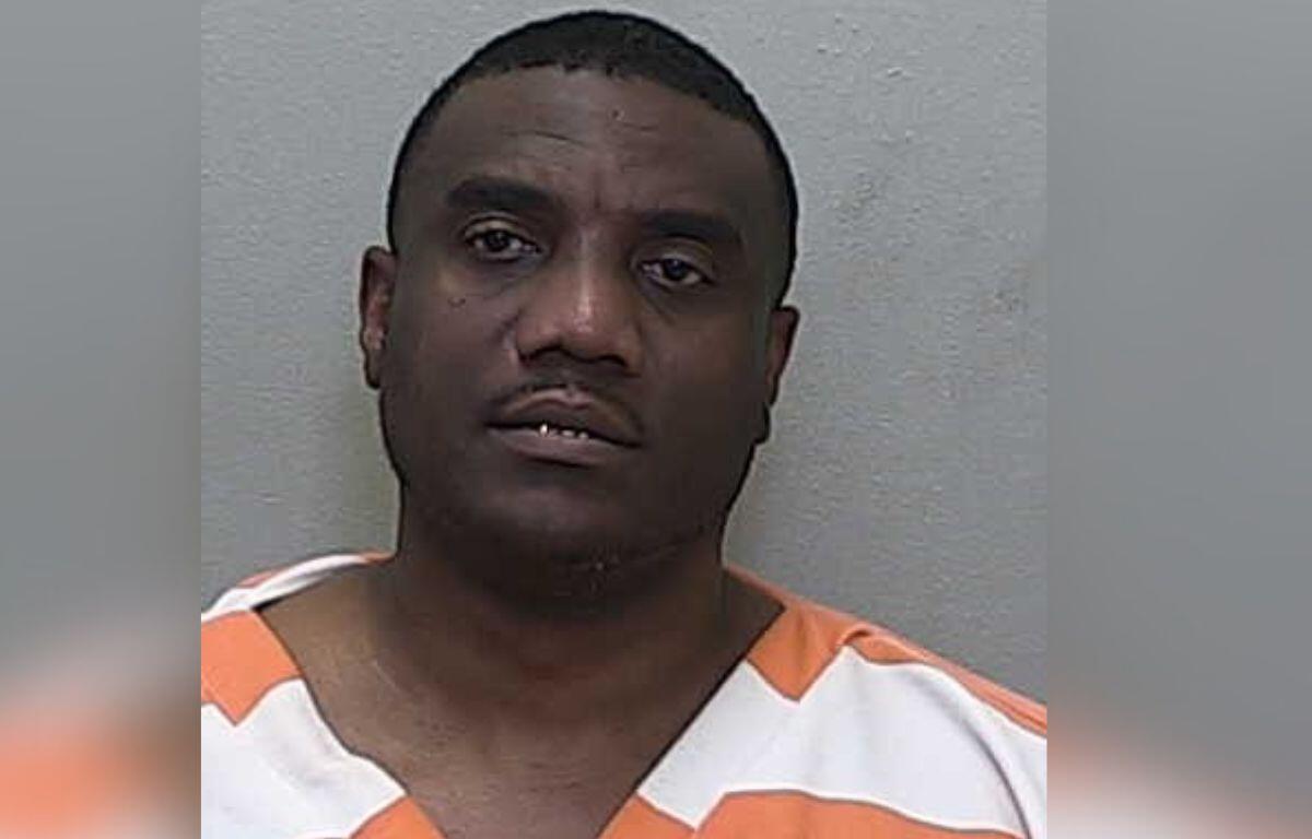 A man wearing a orange and white jump suit standing against a gray wall,