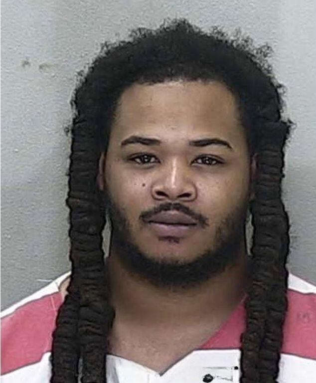 Mugshot of an African American man with long dreads in an orange and white jumpsuit.