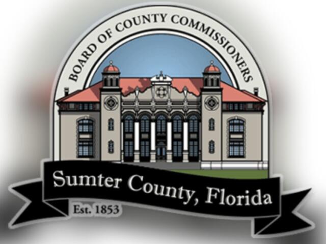 A logo with an arc over top of an image of a building, with lettering in the arc. Below the building, there is a flag banner with writing.