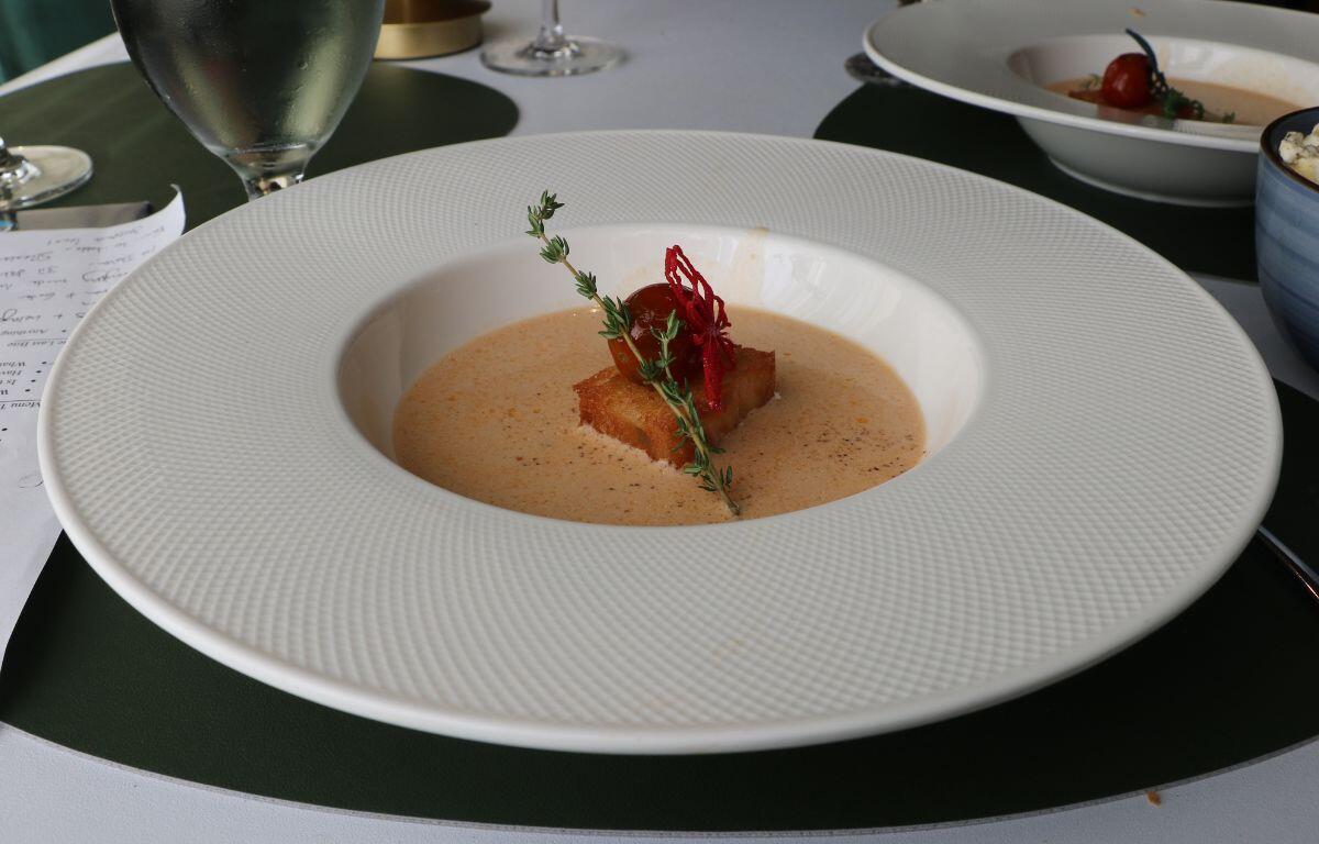 Red-tinted soup in a bowl topped with a green garnish, tomato and crouton.
