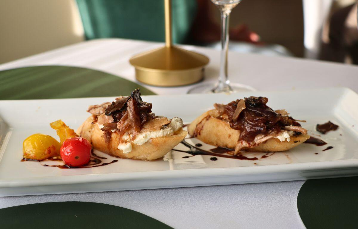 Sliced pork meat with sauce and garnish, resting on slices of baguette.