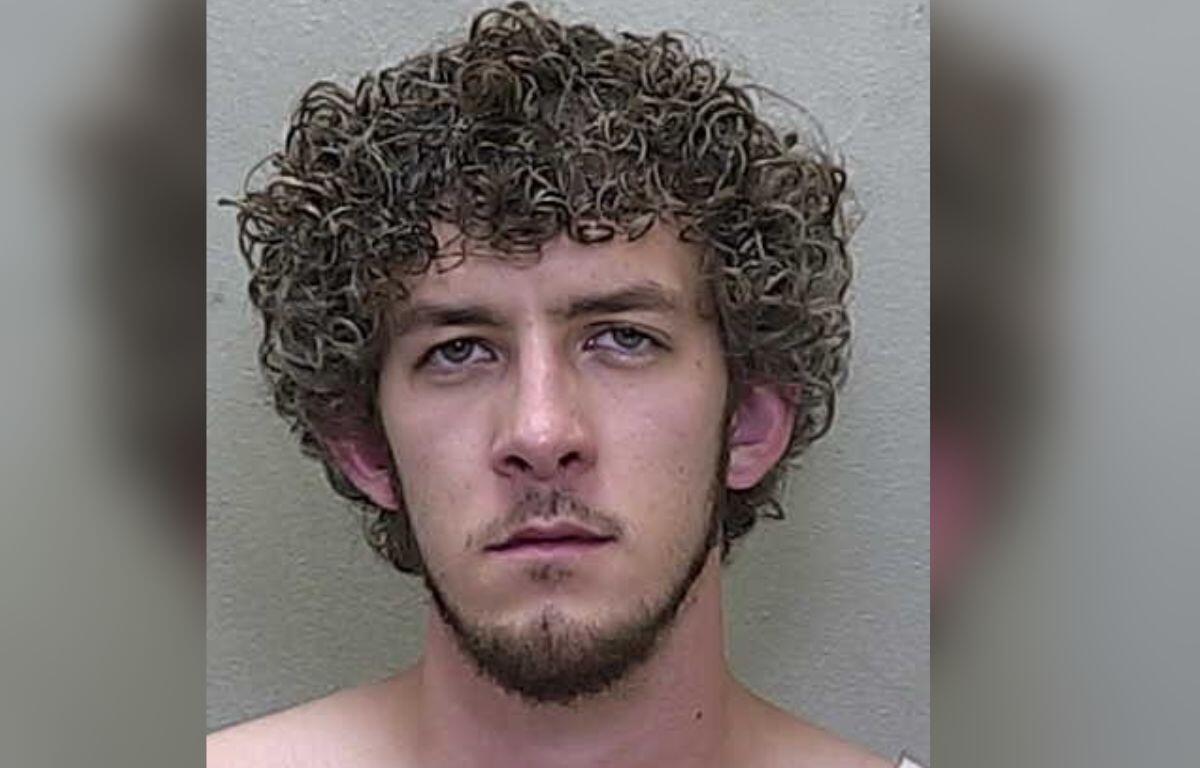 A man in a jump suit standing against a gray wall.