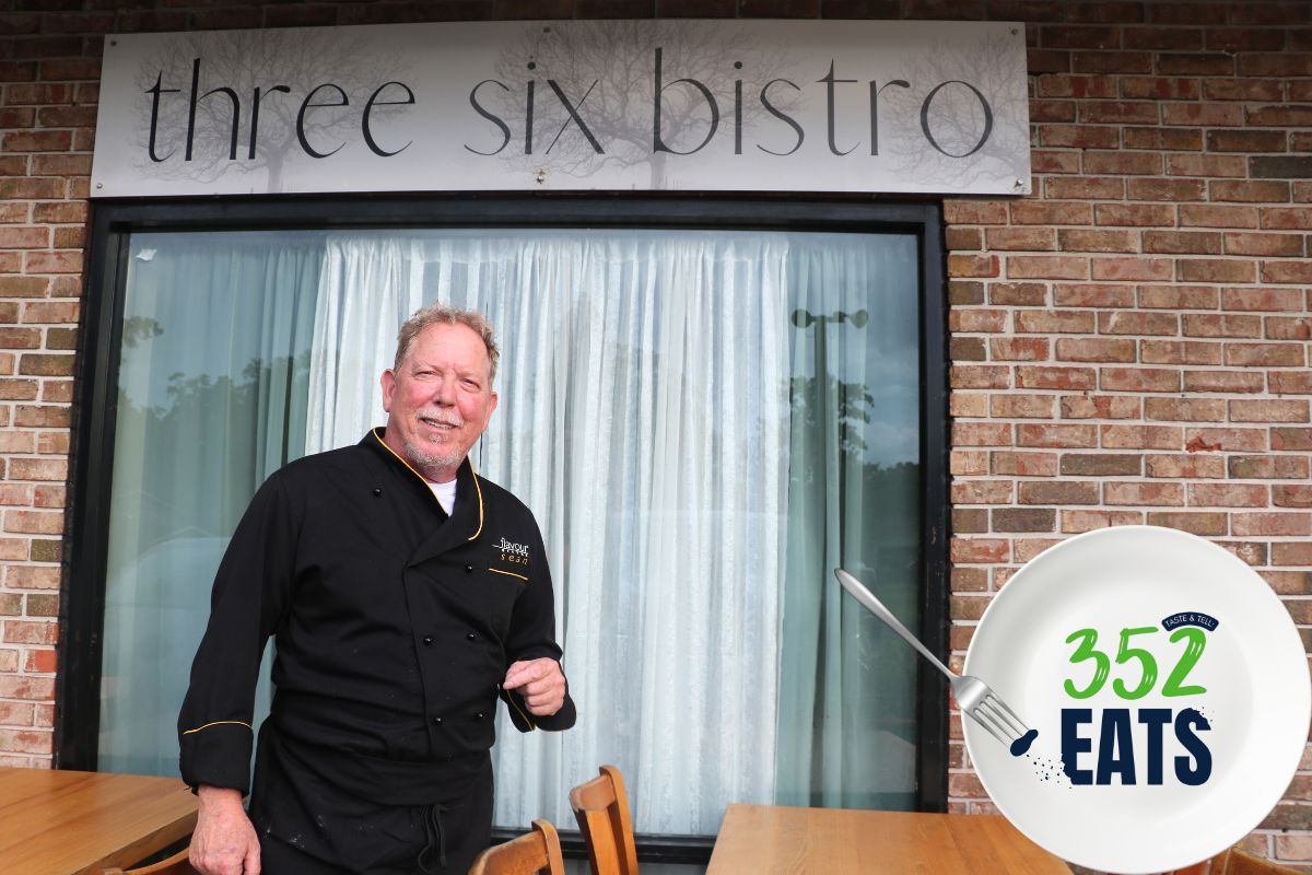 A man in a black chef's uniform standing in front of a brick-front underneath a sign that reads, "Three Six Bistro".