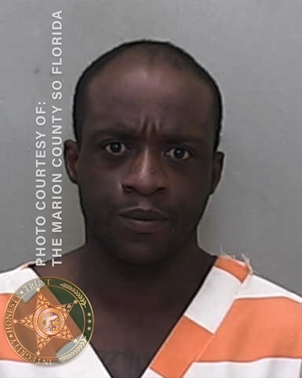 A mugshot of an African American man with receading hair and no facial hair in an orange and white striped jumpsuit against a neutral background.