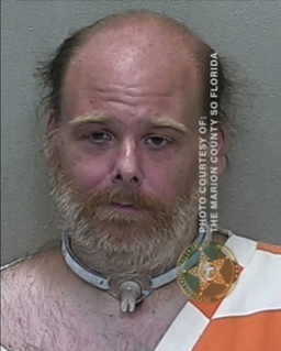 Mugshot of William Fuller, a balding man with a reddish-brown beard and tired eyes, wearing a white-and-orange jail uniform, appearing somber against a gray background.