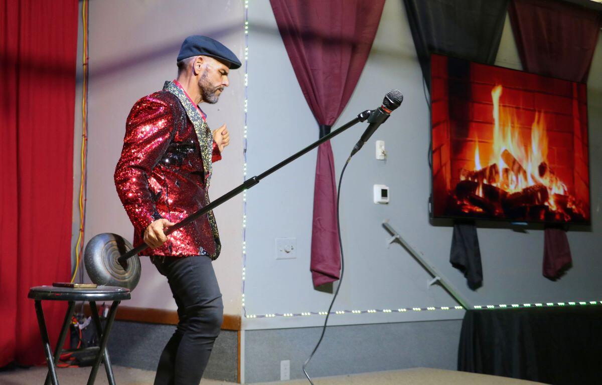 The host stands with a microphone, using expressive gestures as he engages the audience.