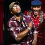 Two performers stand together onstage during the show’s closing, smiling as the night winds down.