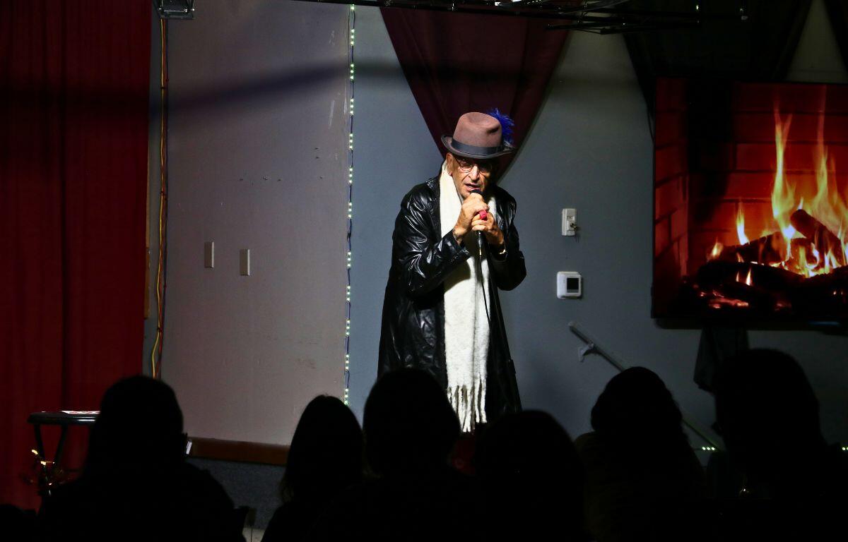 A comedian in a suit entertains a packed audience with bold gestures onstage.