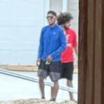 Two men walking outside, one wearing a blue shirt and the other in red, near a residential area.