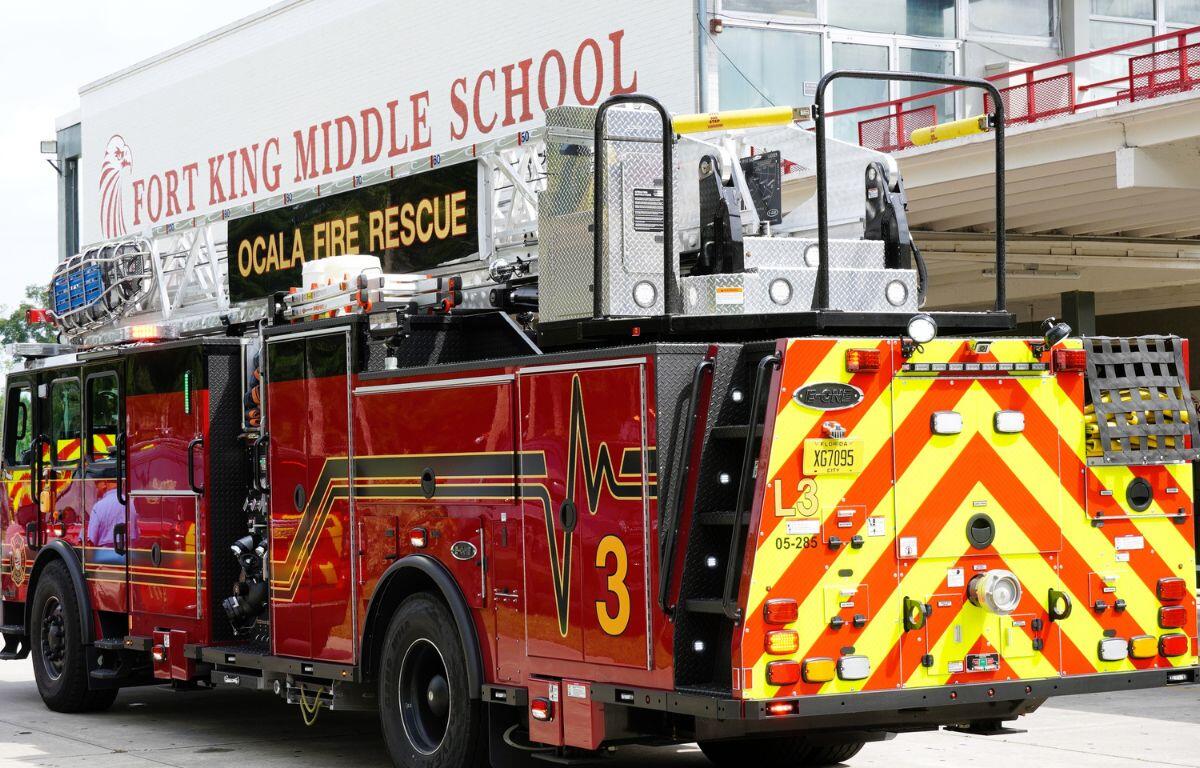 A red fire truck in front of a structure with writing on the facade, and a widow on the right of the structure.